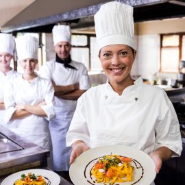Group of chefs holding plate of prepared pasta in kitchen at hotel